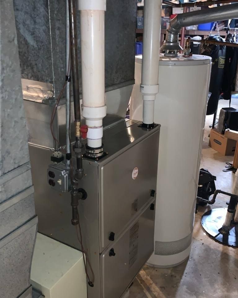 Furnace and water heater in a basement. Metal appliances with white PVC pipes.