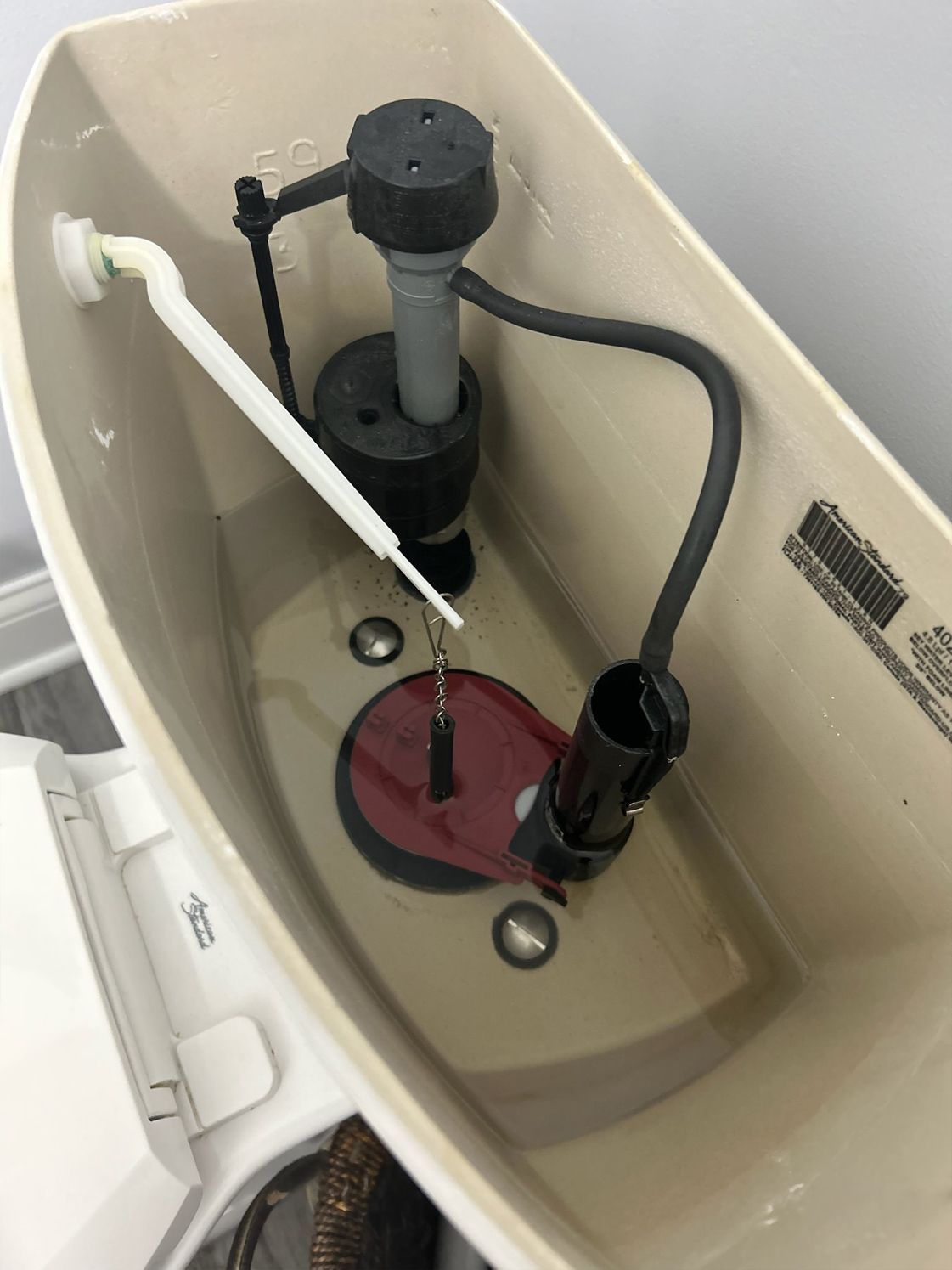 Toilet tank interior showing a fill valve, flapper, and float arm. Brownish-beige tank.