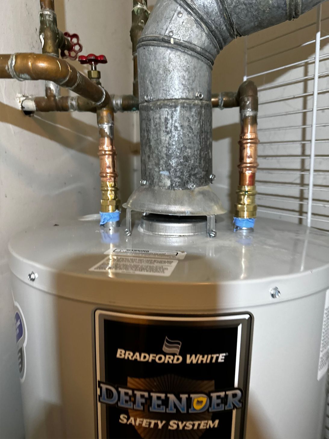 Water heater with copper pipes and vent; Bradford White Defender brand.