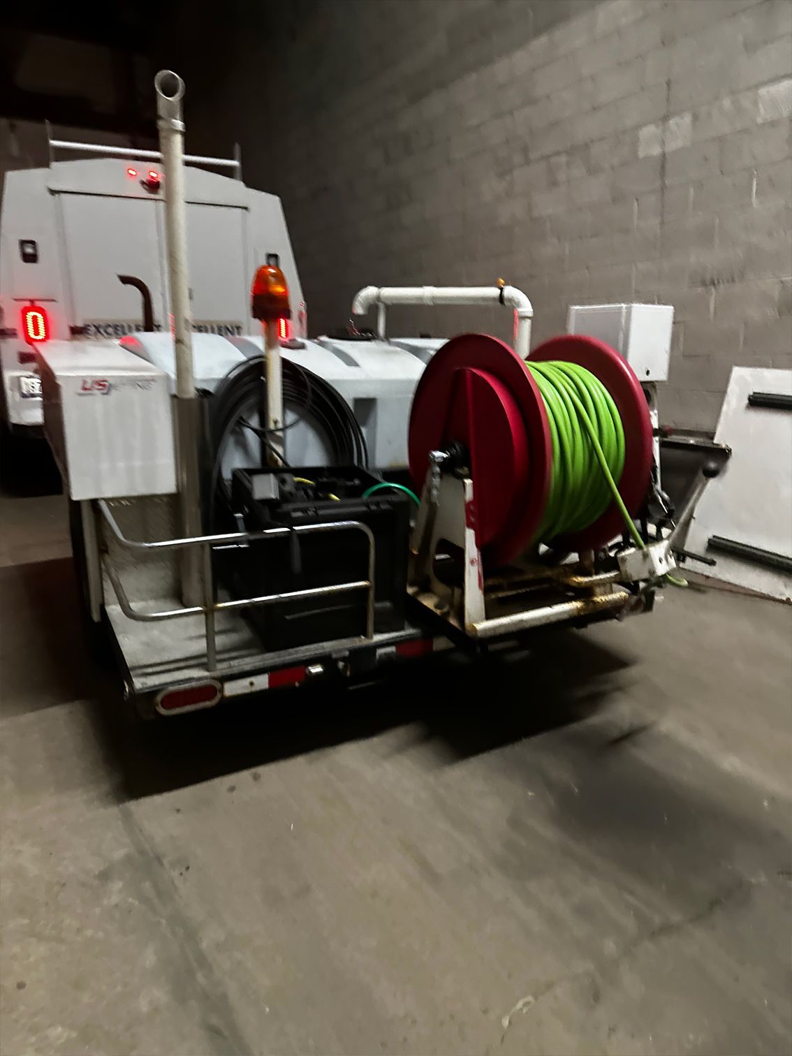 A white trailer with a large red hose reel, and a green hose. An orange light is visible.