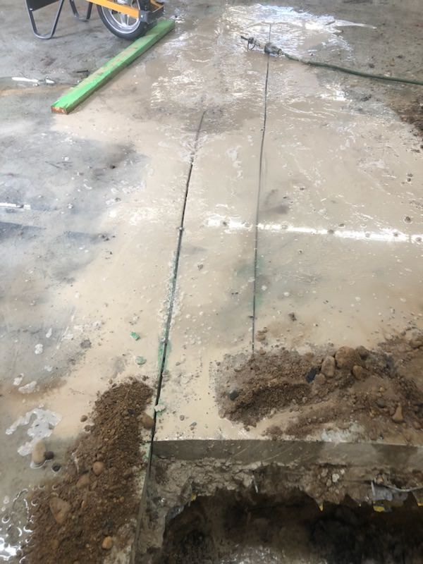 Concrete floor being cut with a saw, water and debris visible.