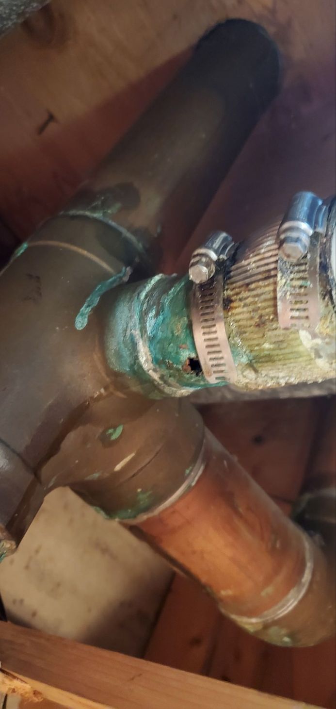 Copper plumbing pipes with heavy corrosion and a hole. Clamps are visible.