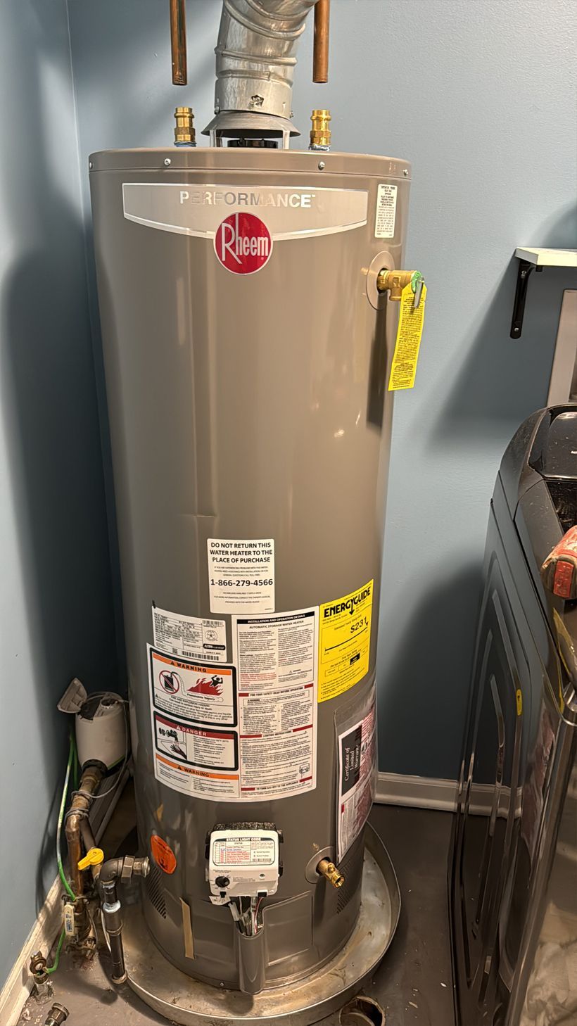 A tall, gray Rheem water heater in a utility room; copper pipes and yellow labels visible.