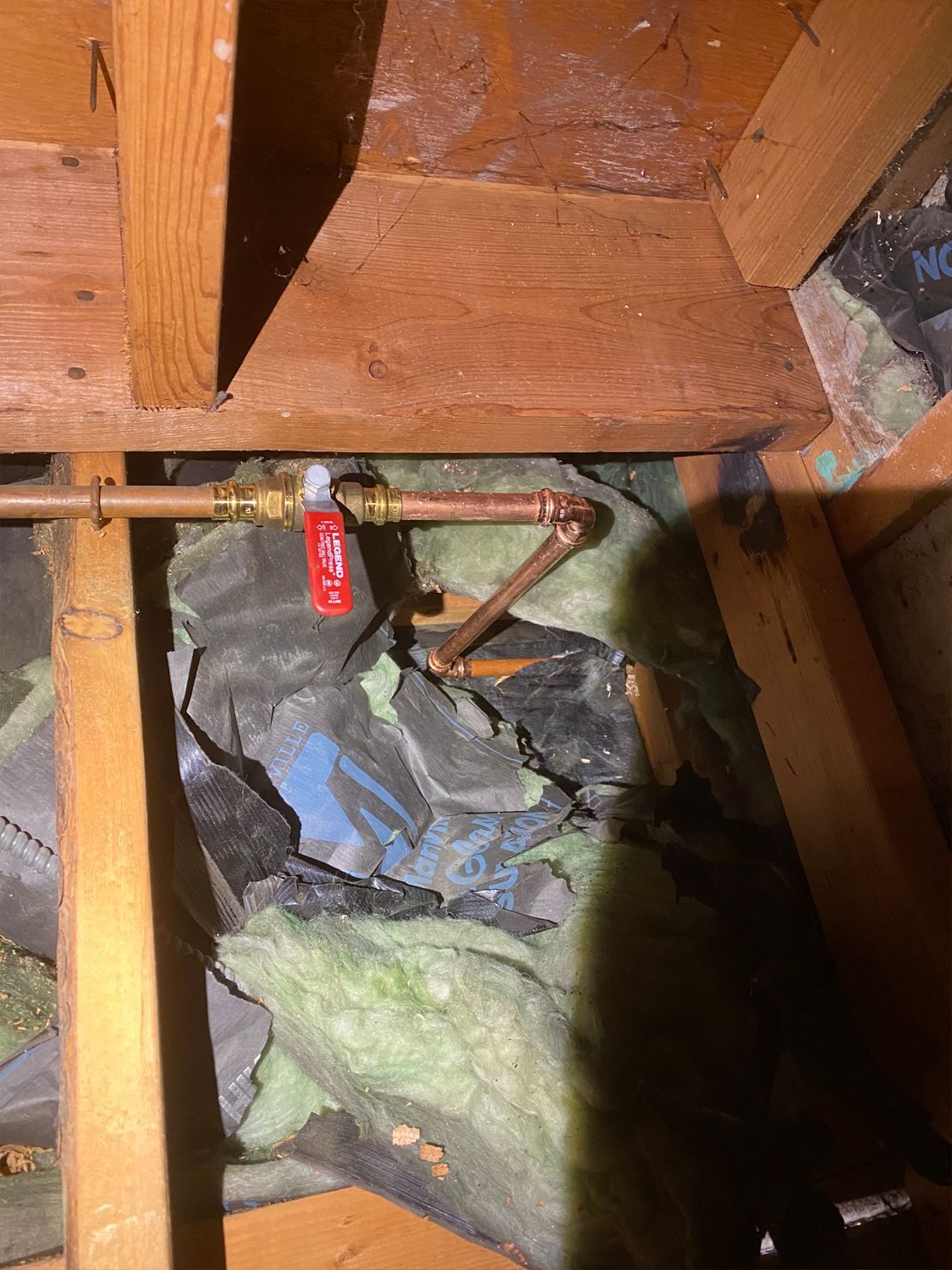 Copper pipes and insulation in an attic. A red tag hangs from a pipe.