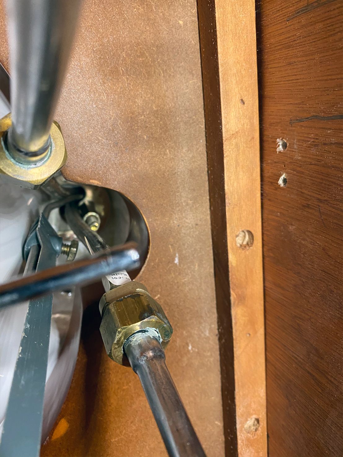 Close-up of plumbing under a sink. Copper pipes with brass fittings are connected, and a wrench is being used.