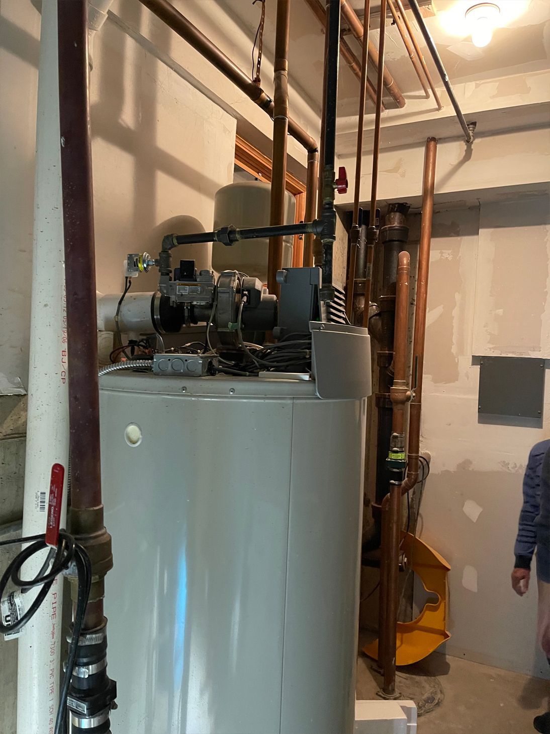 Water heater in a basement with copper pipes and a partially visible person.