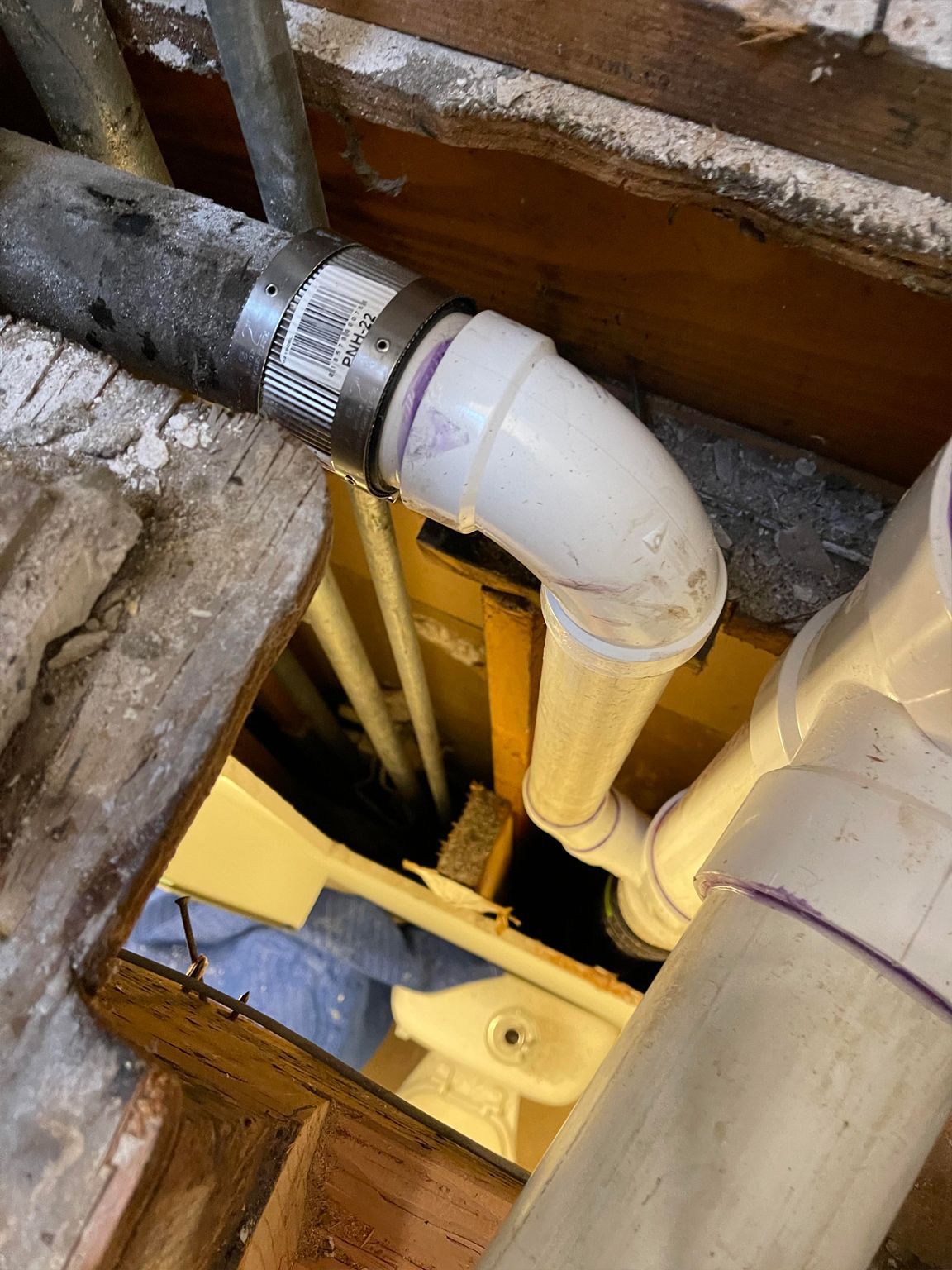 PVC plumbing pipes joined with a clamp and elbow, viewed from above a crawlspace opening.