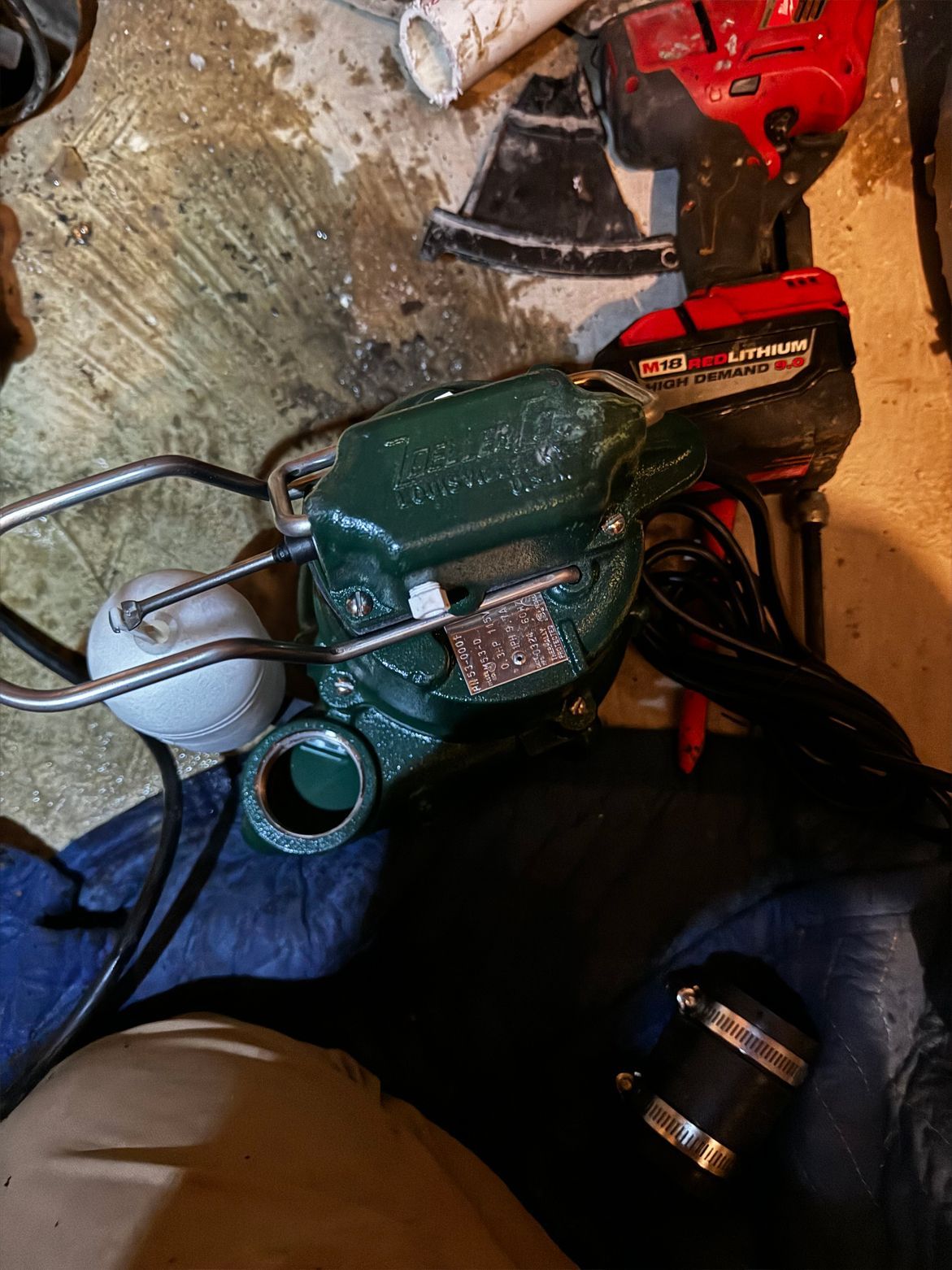 Green sump pump with white float, tools in a basement.
