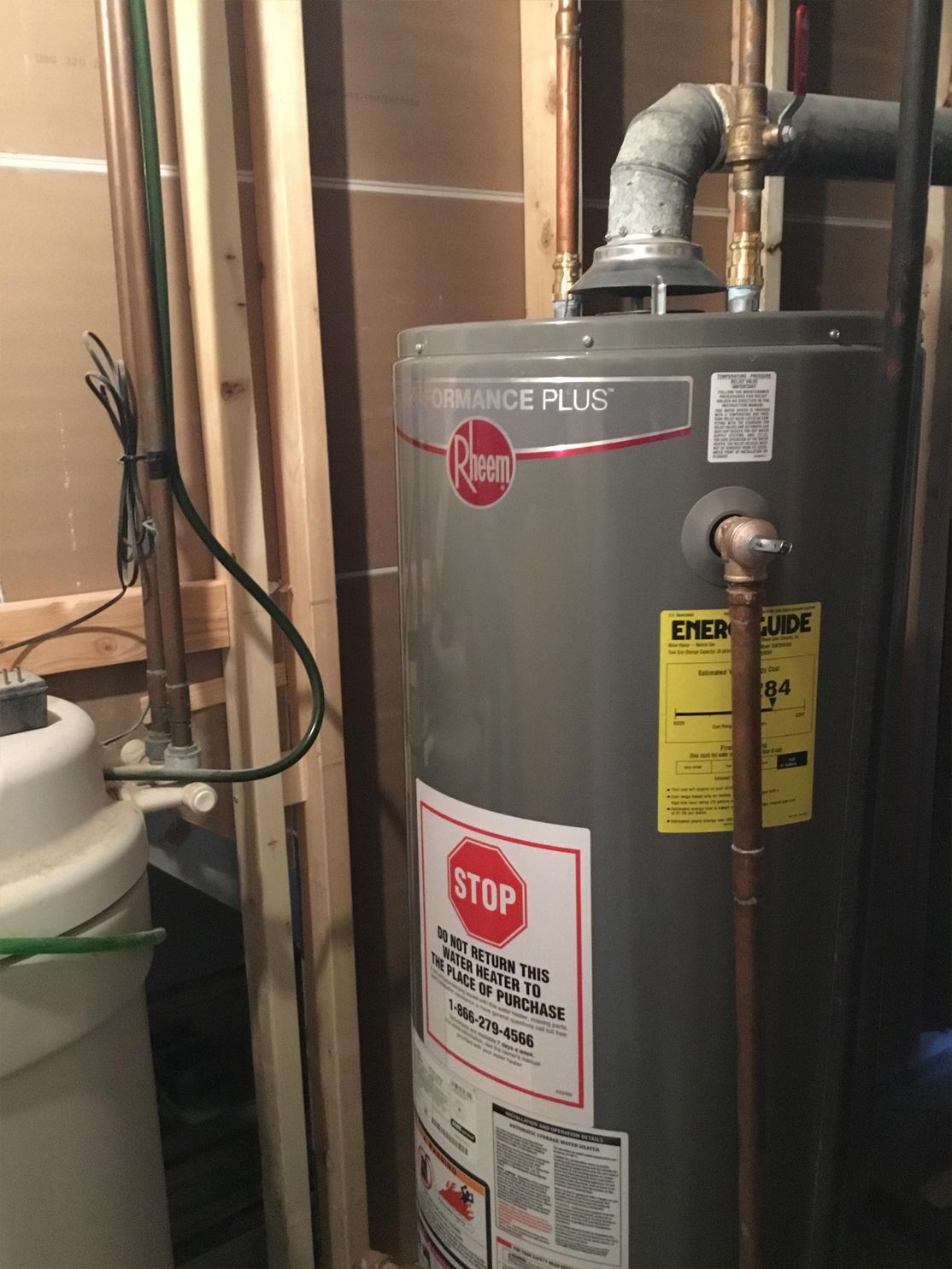 A Rheem water heater in a utility room; pipes and vent visible.