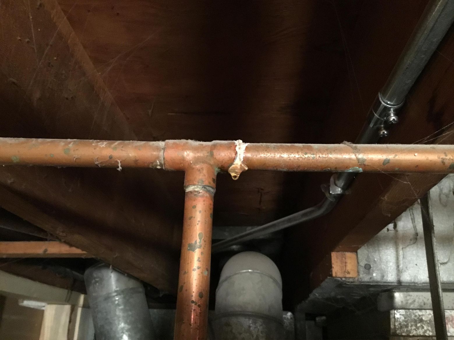 Copper pipes with a leak under a wood ceiling.