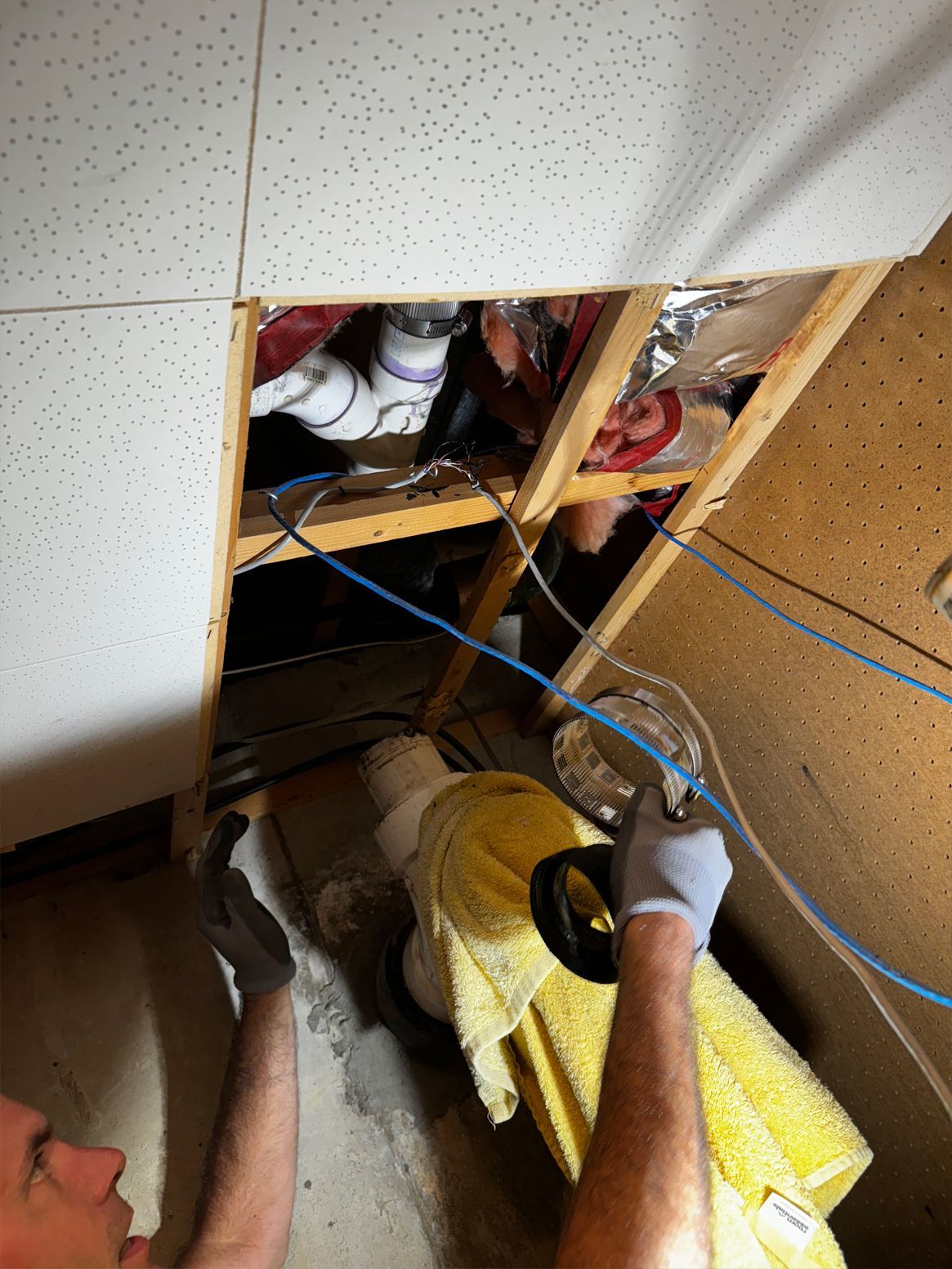 Person looking up into an attic through a ceiling panel, holding a flashlight and pulling a blue cable.