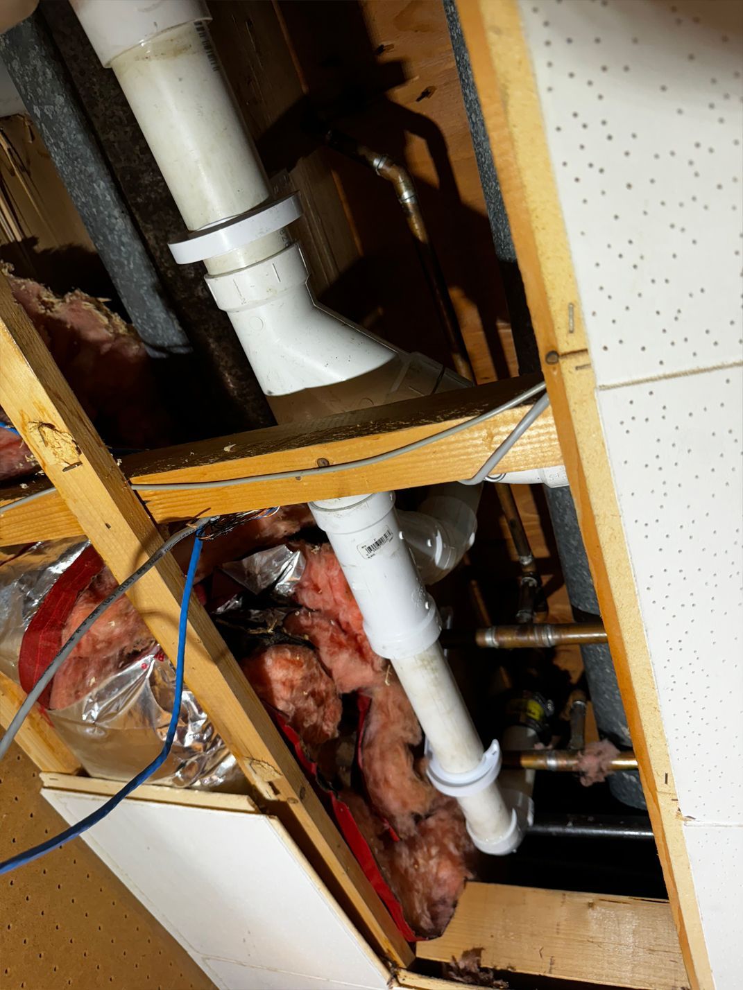 White PVC pipes and ductwork within a wooden ceiling framework, surrounded by insulation.