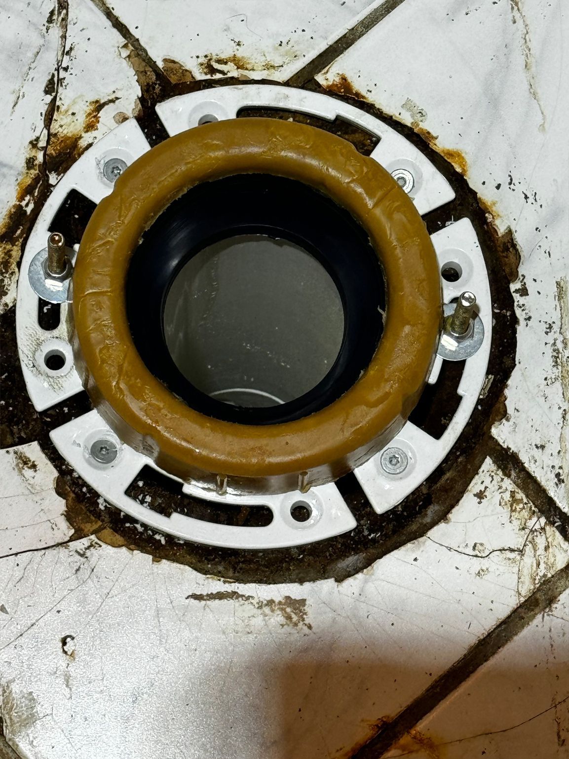 Toilet flange with a wax ring and mounting bolts on tiled floor.