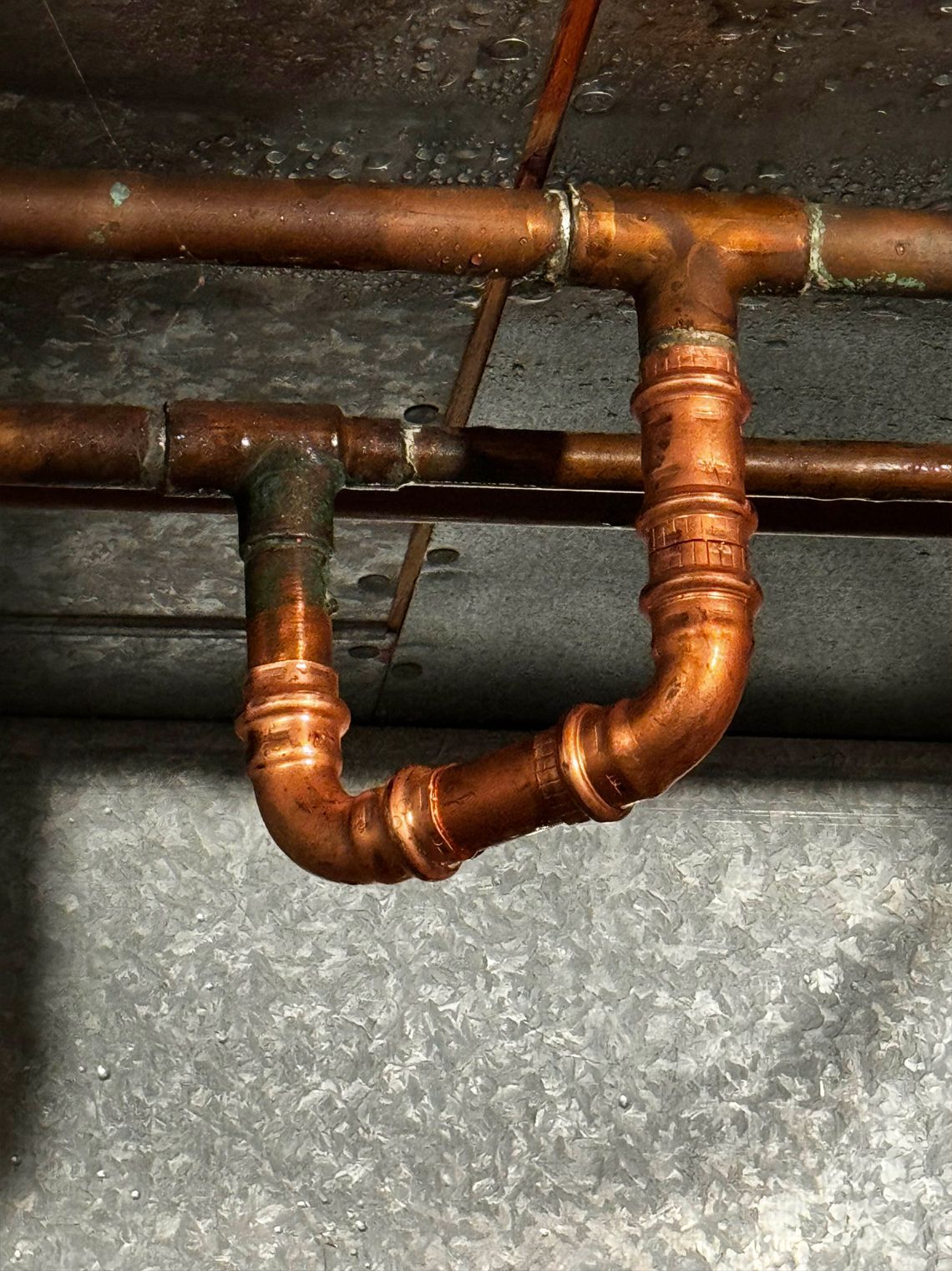 Copper pipes in a U-shape, connected with joints, on a gray metal surface.