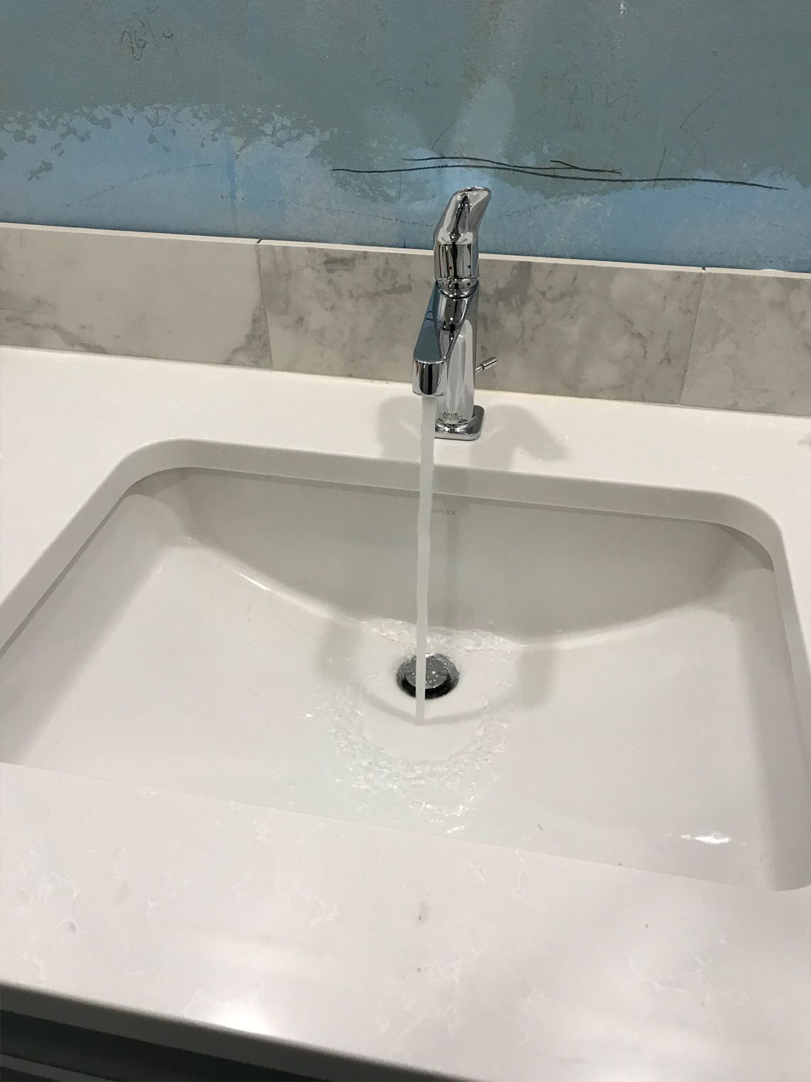 White bathroom sink with running water, chrome faucet, and marble countertop.