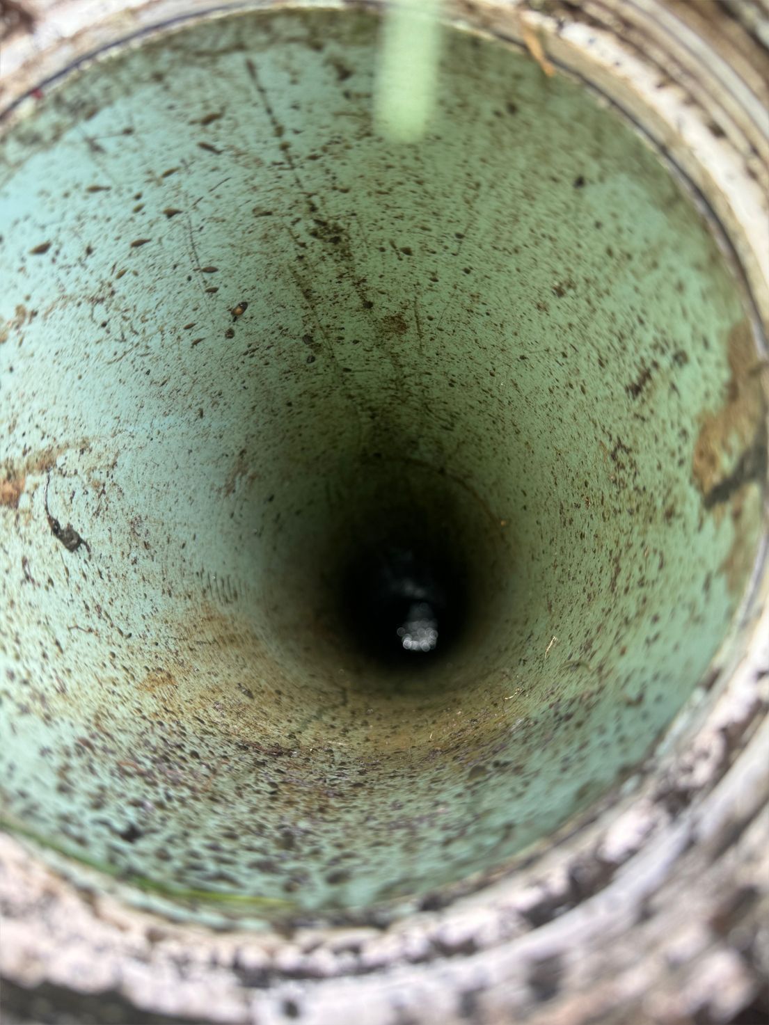 Looking down into a light teal-colored pipe with dark interior, mossy with grime.
