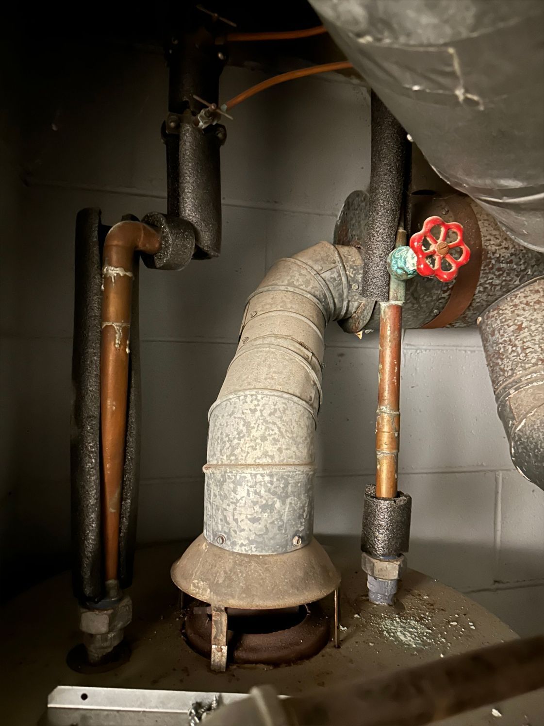 Pipes and a furnace vent in a dark, possibly industrial setting; some pipes are insulated.