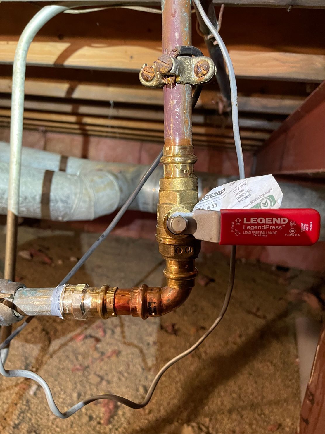 Copper pipe with a red handled ball valve in a crawl space.