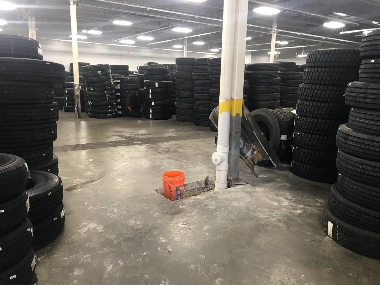 Warehouse filled with stacks of tires. Gray concrete floor, white support columns, bright overhead lights.