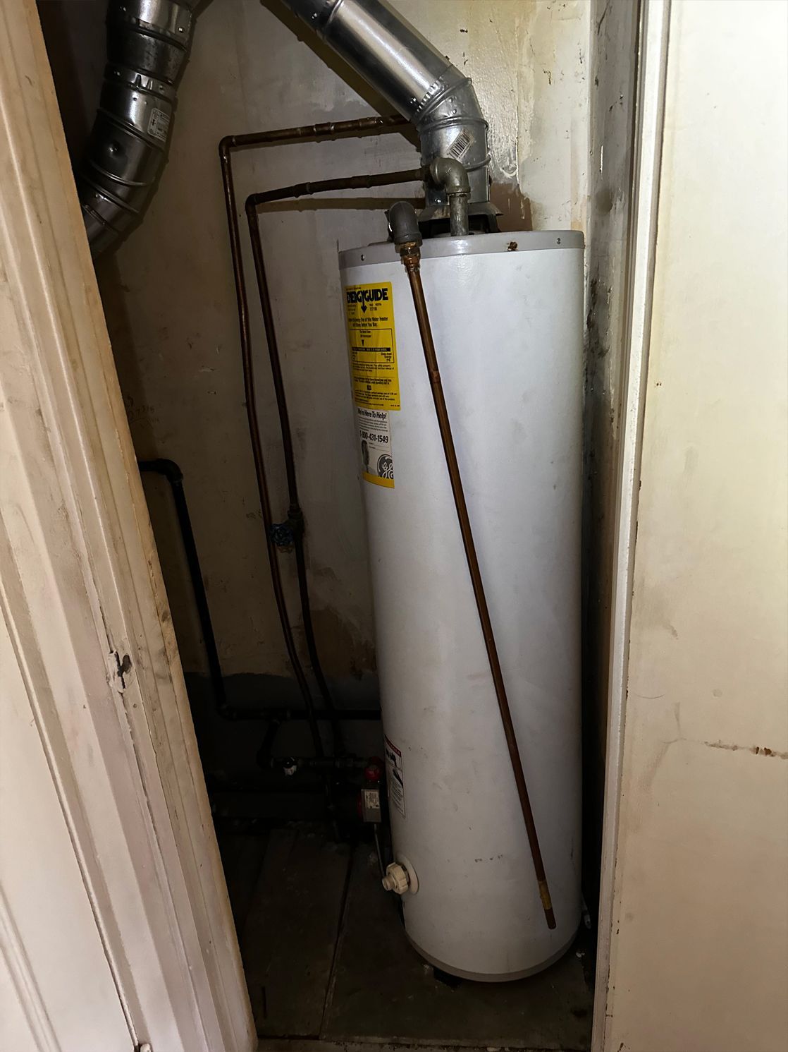 Water heater inside a small, enclosed space, with visible pipes and vent.