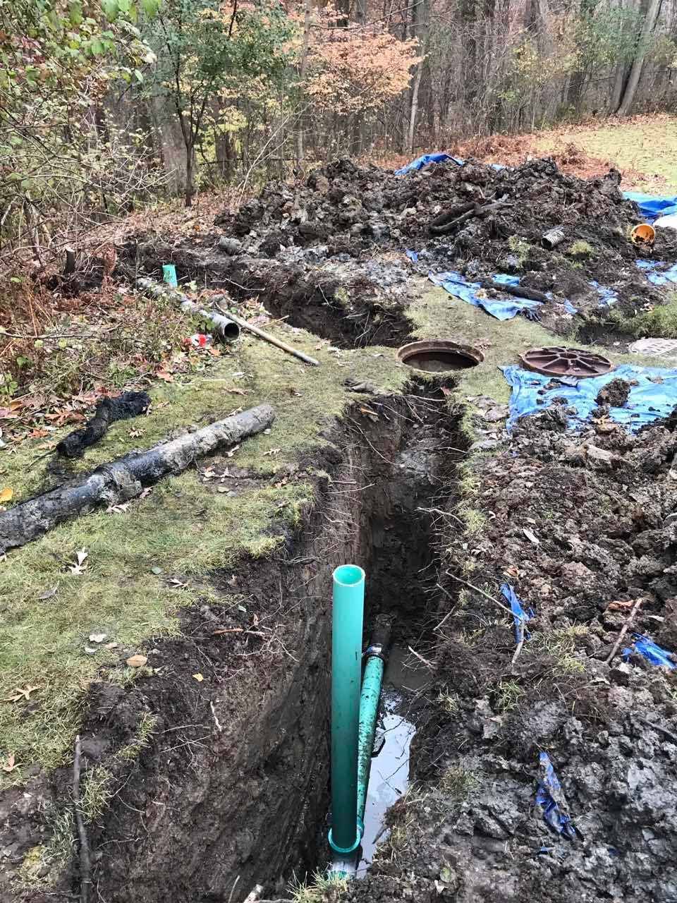 Trench dug in yard with green pipes and exposed dirt, likely for plumbing work.