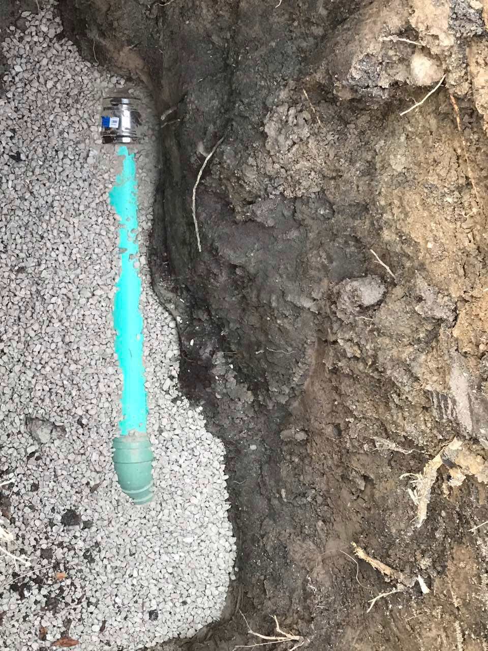 Green pipe and valve in a trench, next to dirt and gravel.