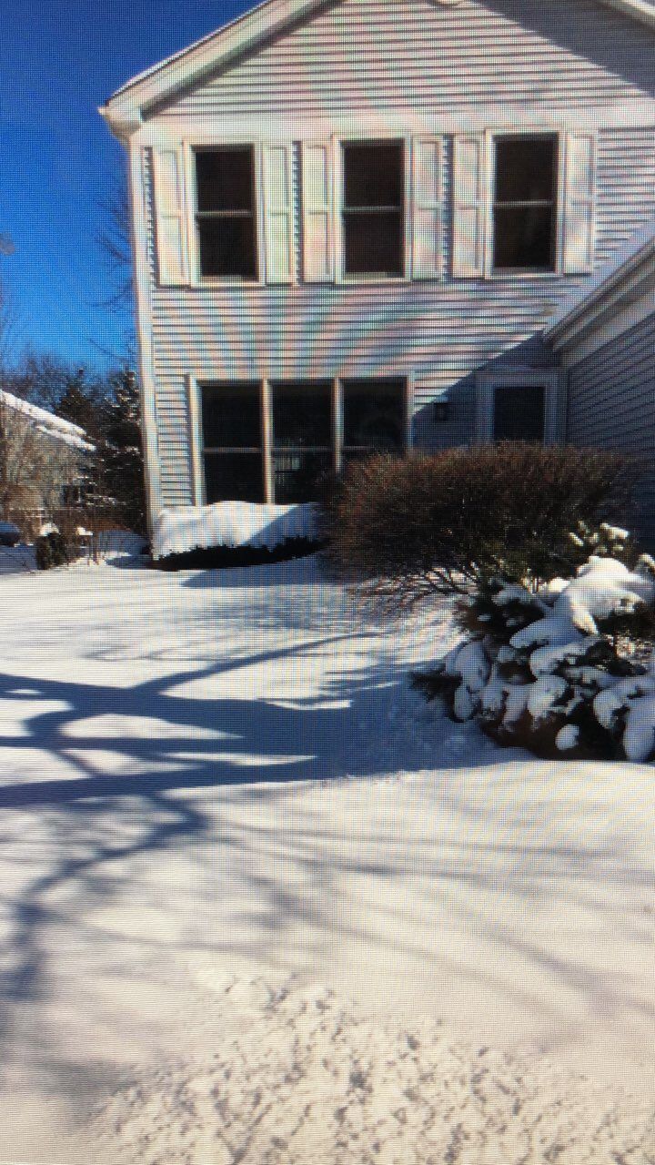 Two-story house with snow-covered lawn and bushes. Winter scene with shadows.