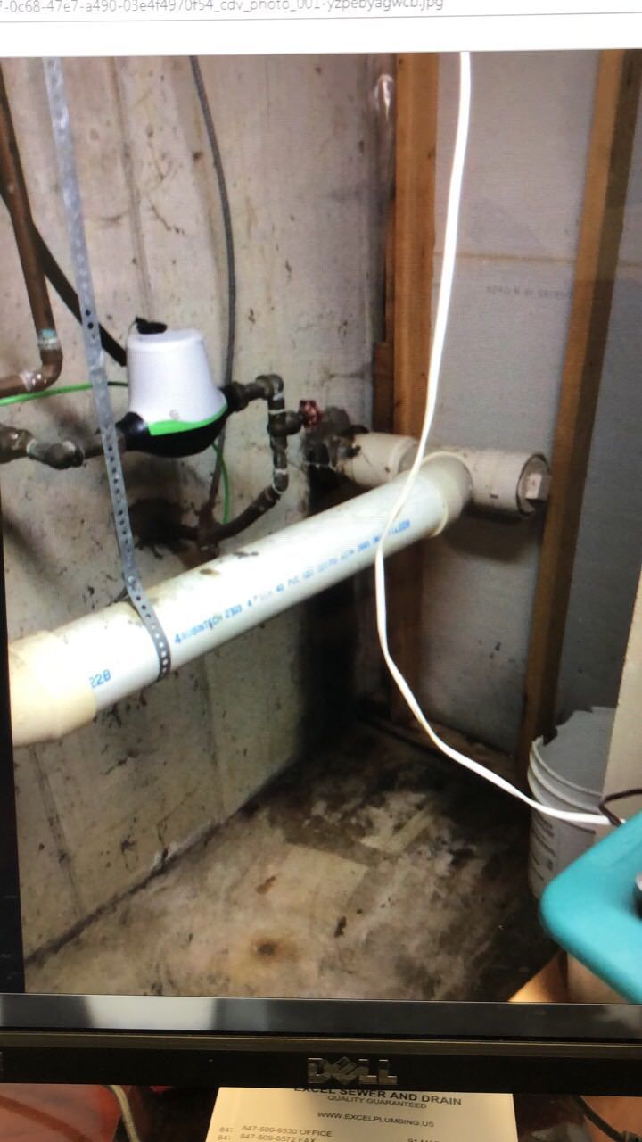 Basement pipes and plumbing with a white PVC pipe and a water shutoff valve. The area is dirty and concrete.