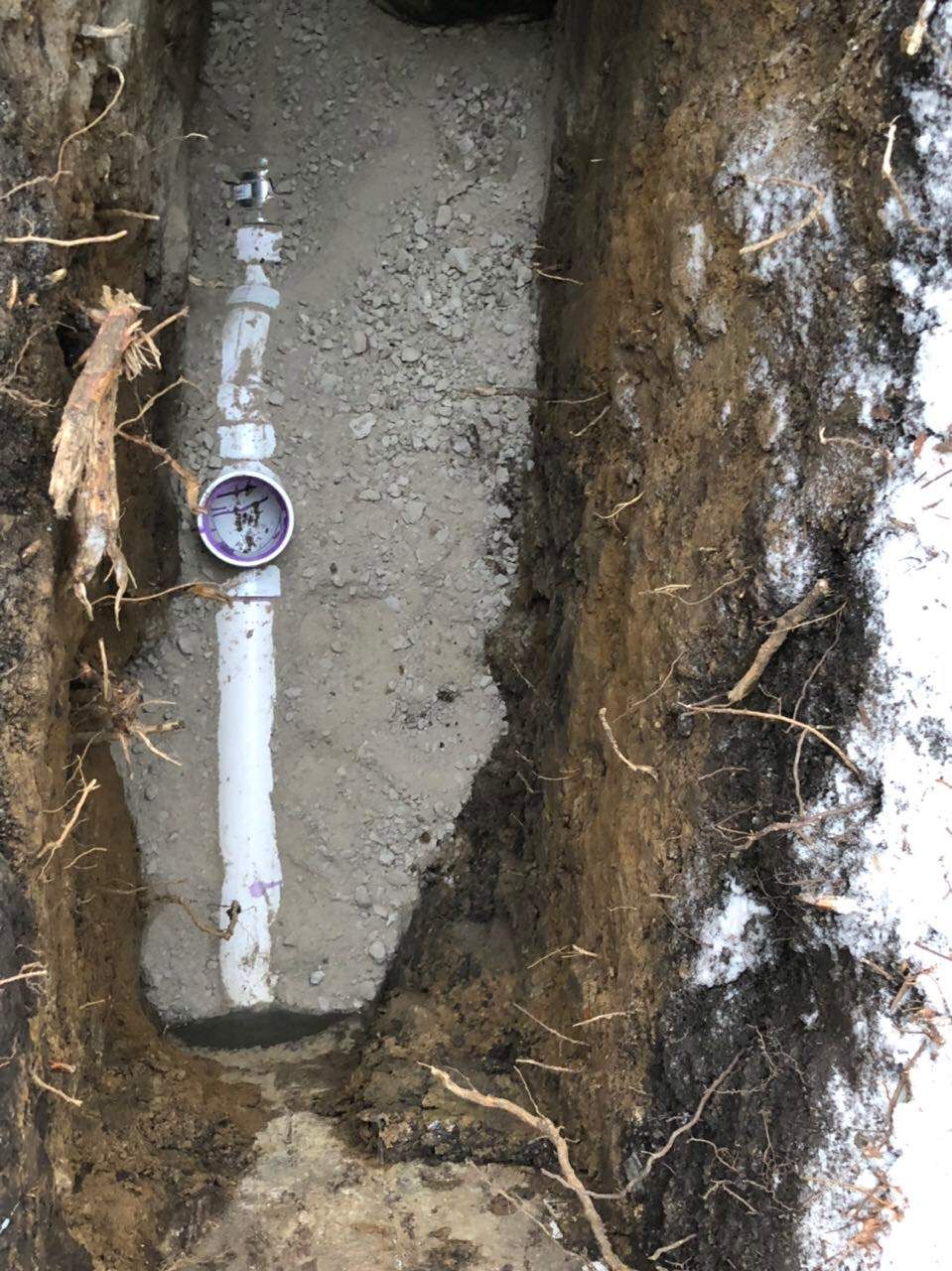 Underground water meter in trench, surrounded by soil and tree roots.
