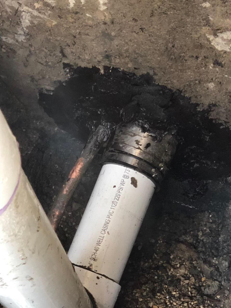 PVC pipe connection within a dark, wet cavity. Black sealant surrounds the connection.