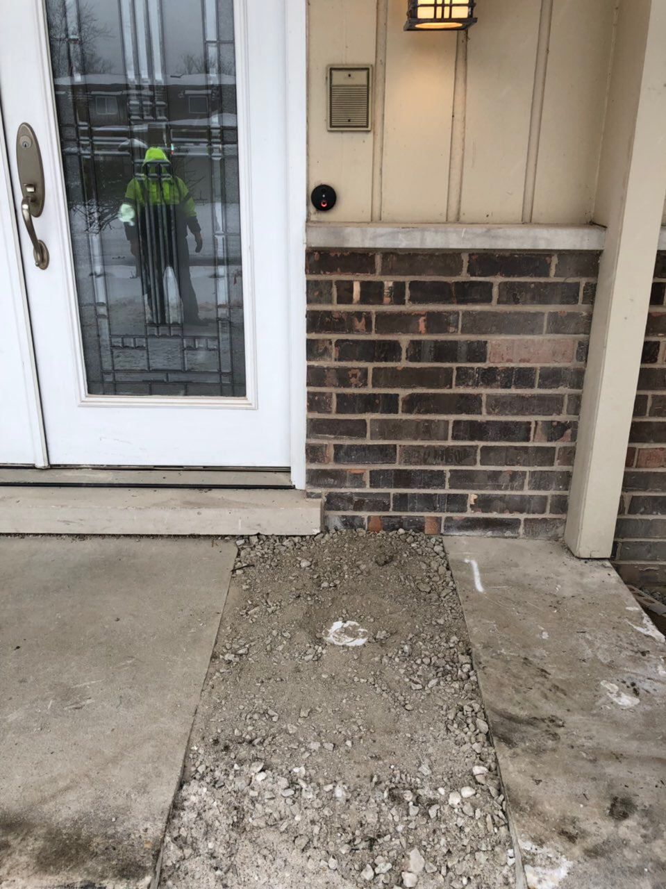 Concrete walkway under construction, next to brick facade and front door.