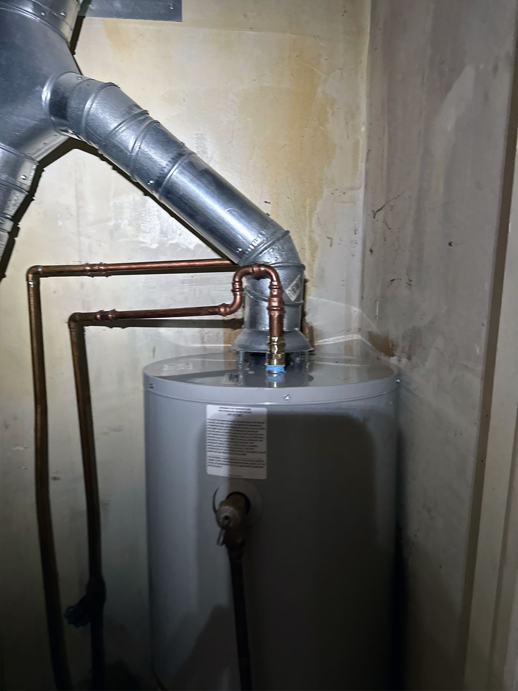 Water heater with copper pipes, vent, and gas valve in a utility room.