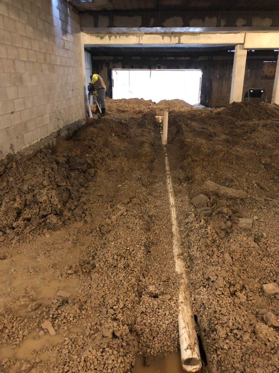 Worker cutting concrete near a buried pipe in a construction site. Dirt piles surround.
