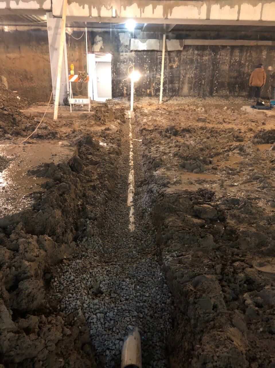 Trench dug in dirt, filled with gravel, and a pipe in the center. Construction site.
