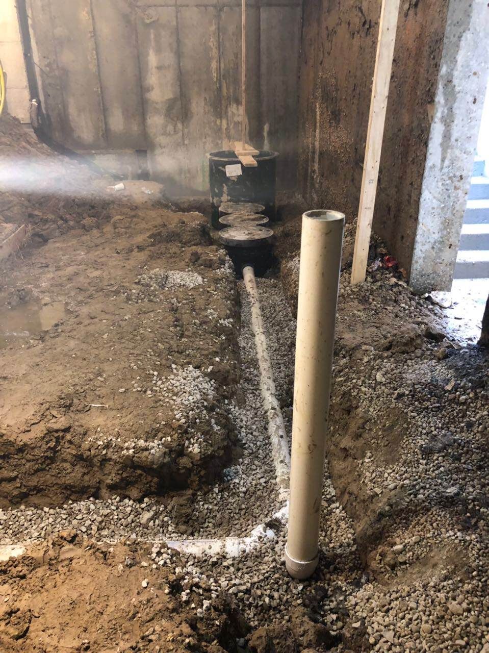 Construction site with a pipe, gravel, dirt, and concrete walls. A vapor rises near a dark cylindrical object.