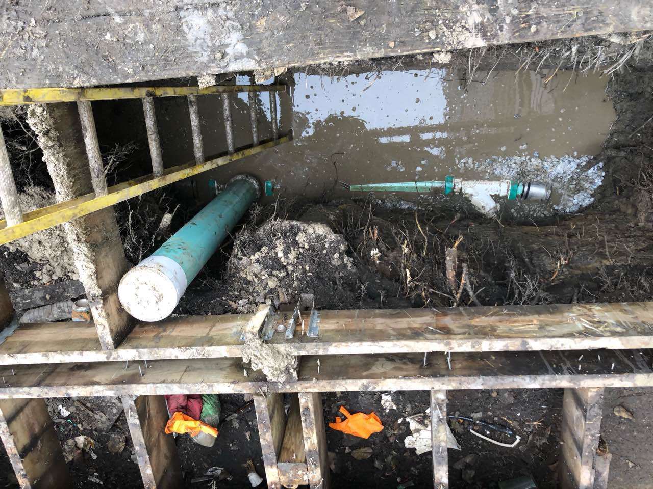Sewer maintenance. A partially submerged work area with pipes, debris, and a ladder.