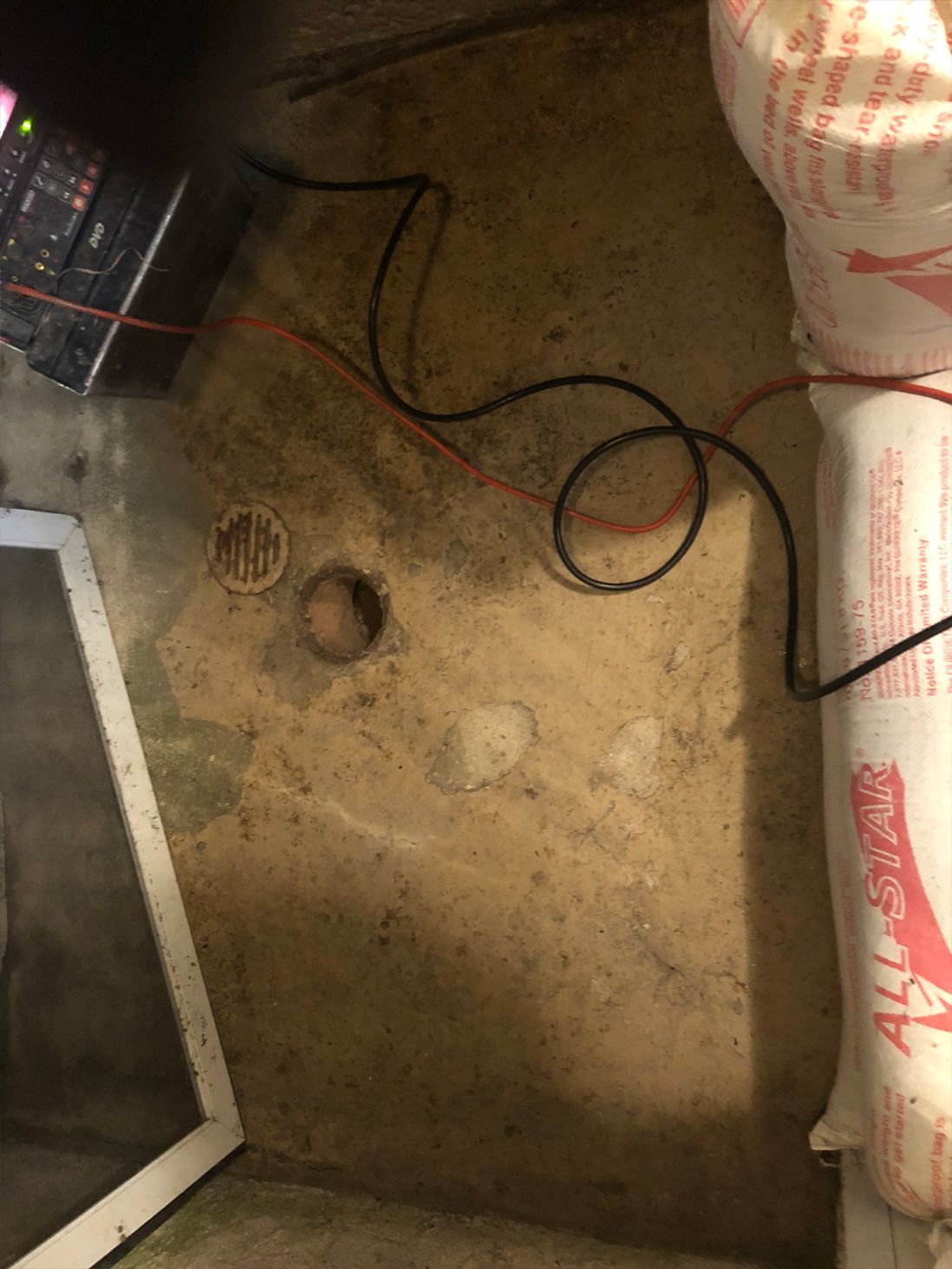 Concrete floor with a drain and wires. Insulation rolls are at the right, a window frame at the left.