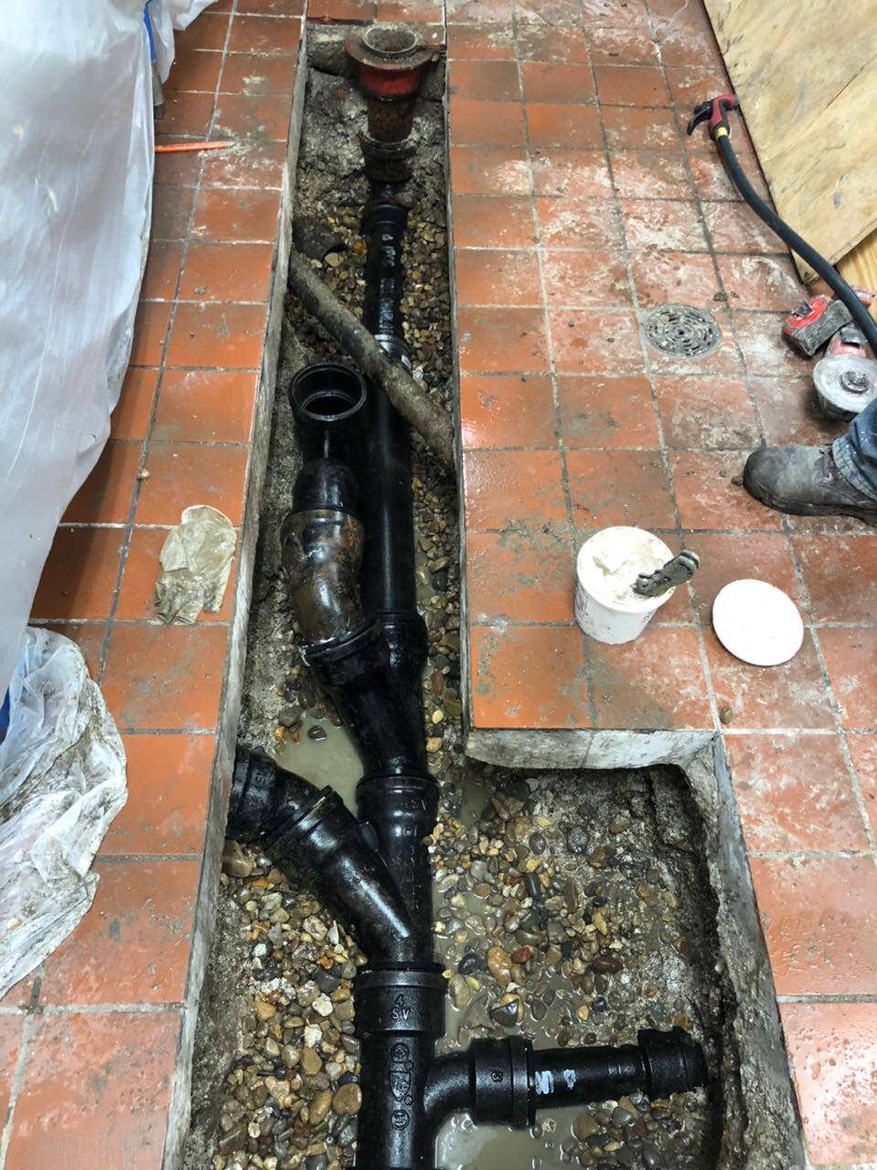 Black plumbing pipes installed in a trench cut in red tile flooring.