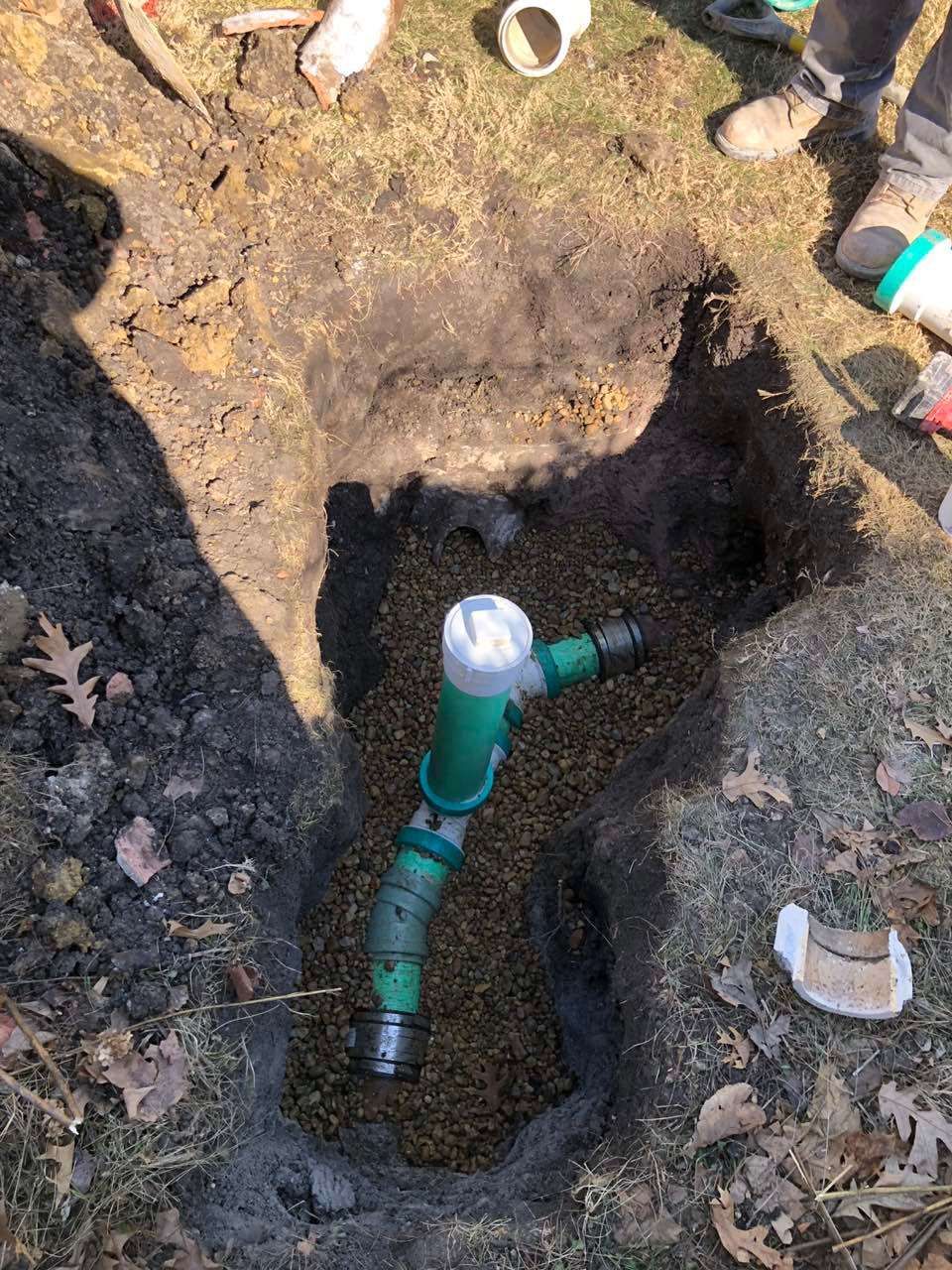 Green irrigation pipe in a dirt pit, being worked on by people. Brown soil, white pipe pieces.