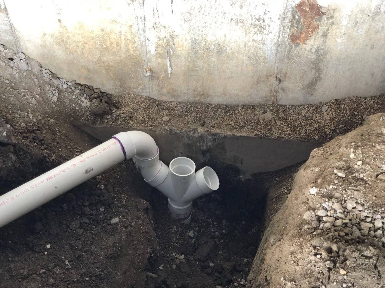 PVC pipe installation with a Y-fitting in a trench next to a concrete foundation.