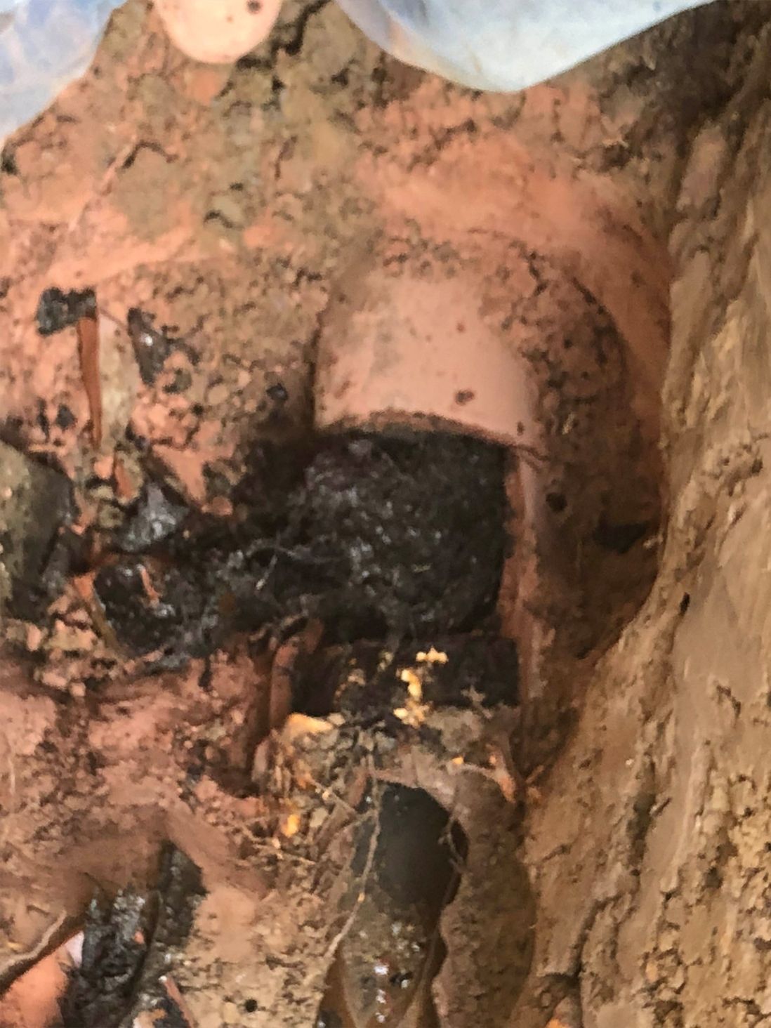 A dark mass of debris surrounds a section of pink pipe in a muddy excavation.