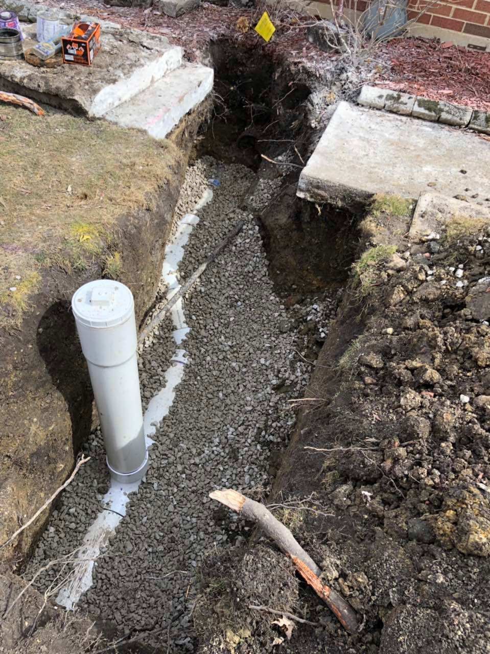 Trench with gravel and pipe, near a concrete step, in an outdoor setting.