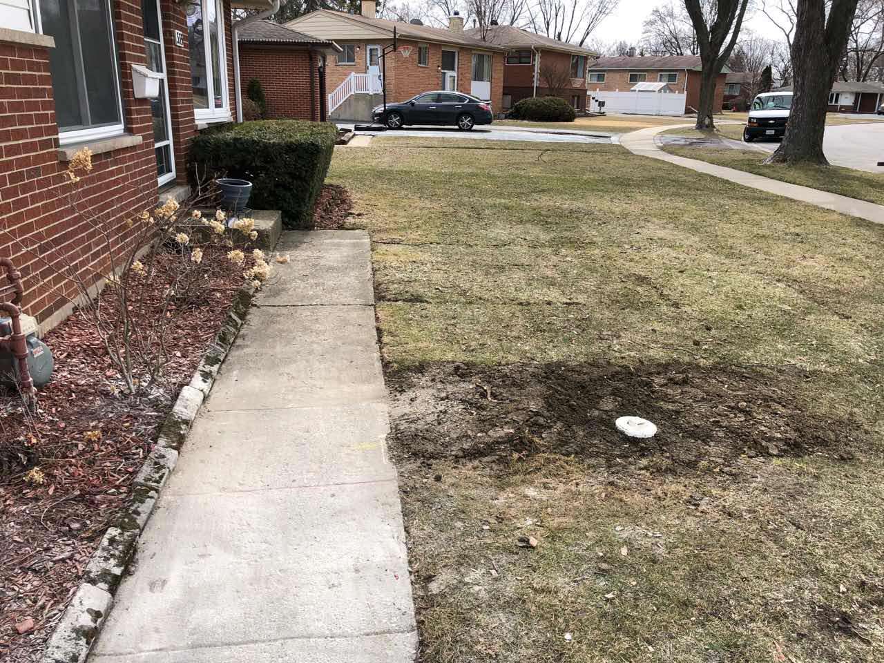 Sidewalk leading from a red brick house to a lawn with sparse grass, cloudy day.