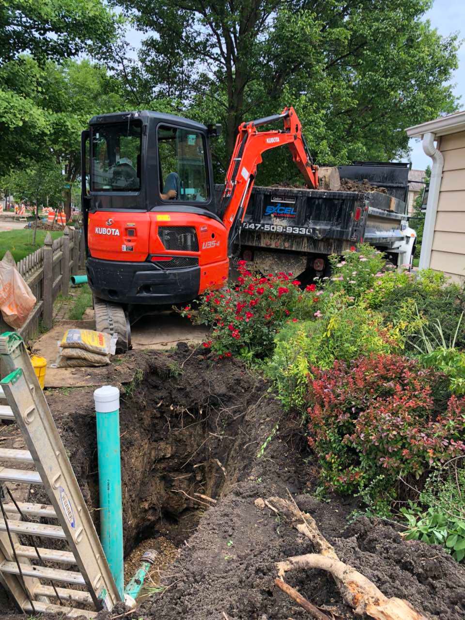 Mini excavator at a construction site, digging near a truck and a house.