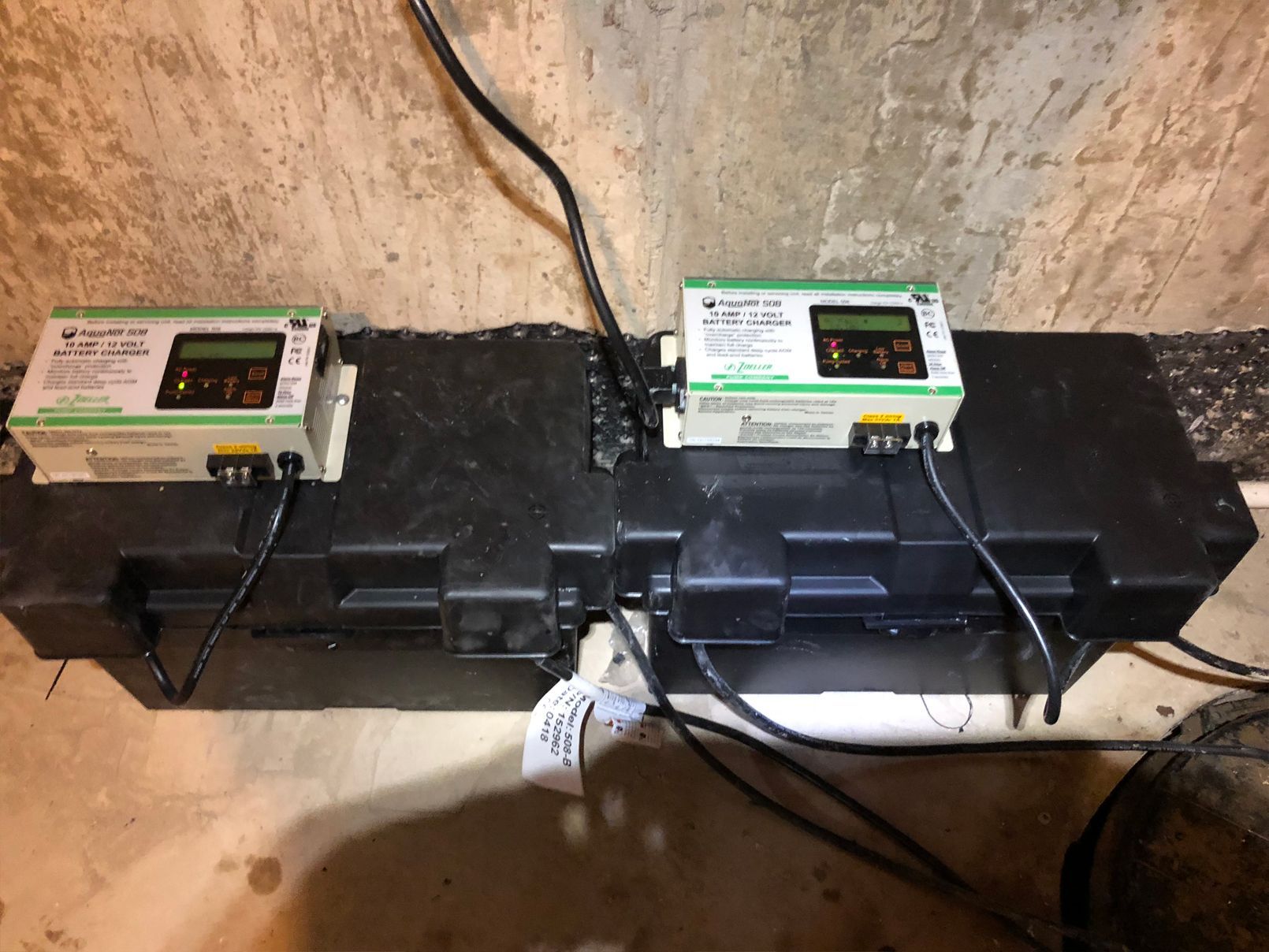Two green-and-white control boxes on a black enclosure, connected by black wires, likely for a sump pump system.
