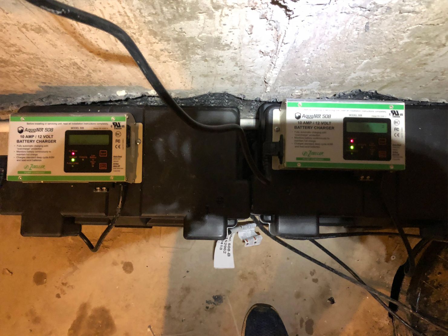 Two green and gray control boxes with LCD screens mounted on a basement wall.