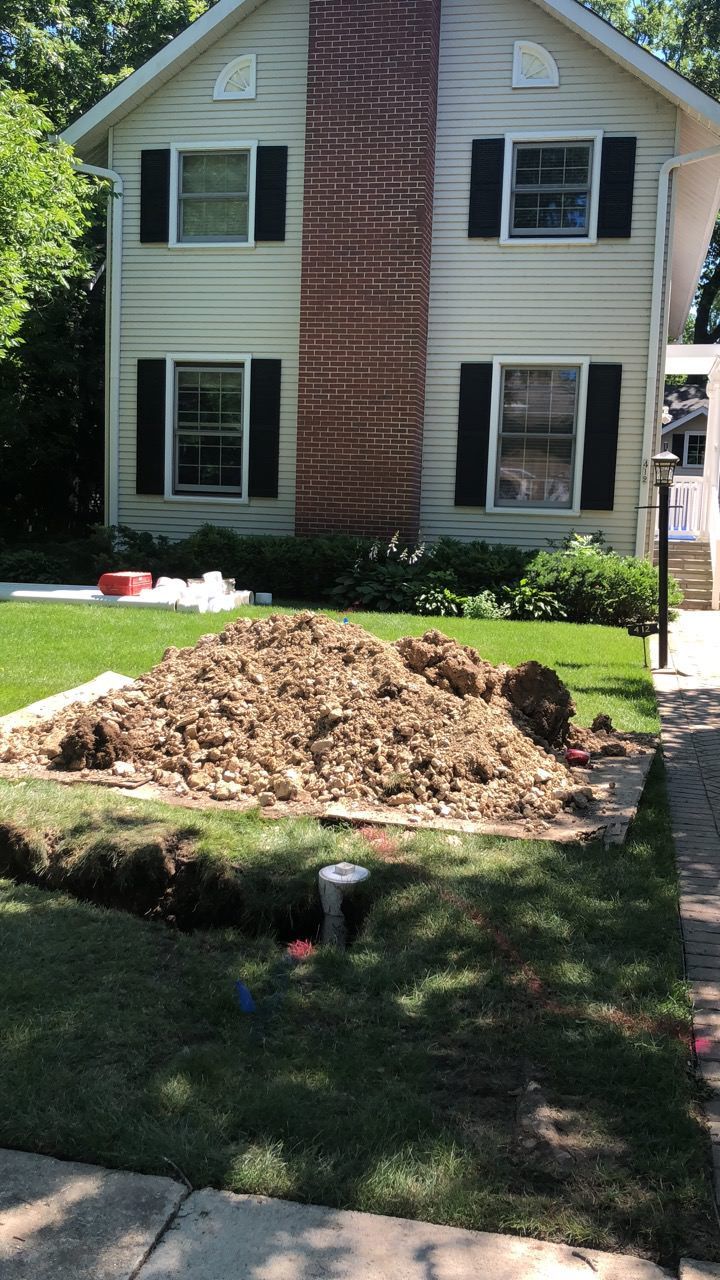A house with a large pile of mulch in a small excavated area in the front yard.
