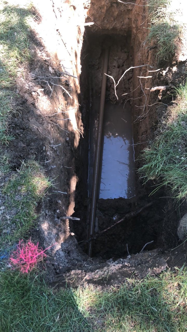 A narrow trench dug in the ground, revealing a concrete structure. Sticks and dirt are visible.
