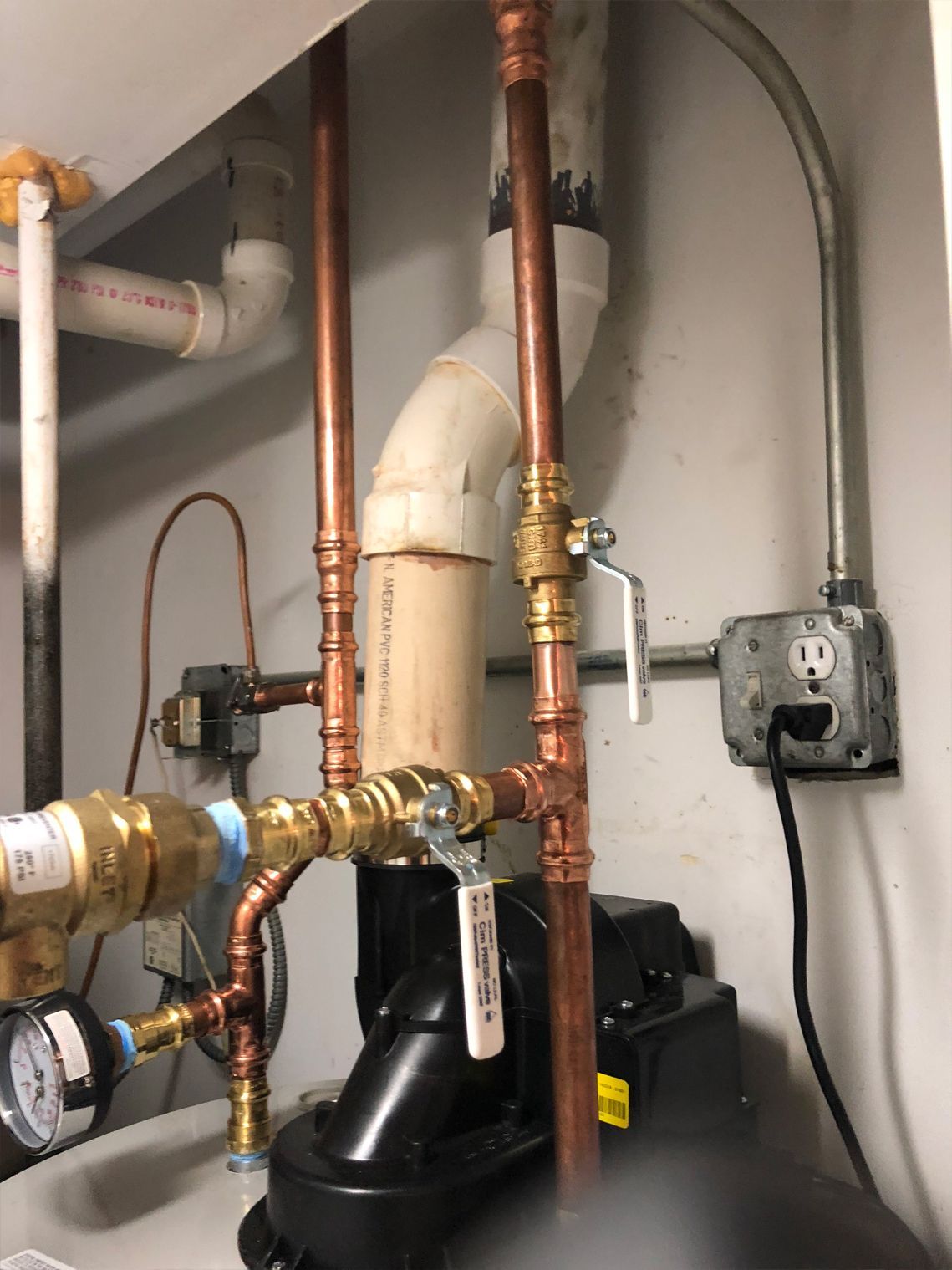 Copper pipes with valves and a pump in an industrial setting, next to an outlet.