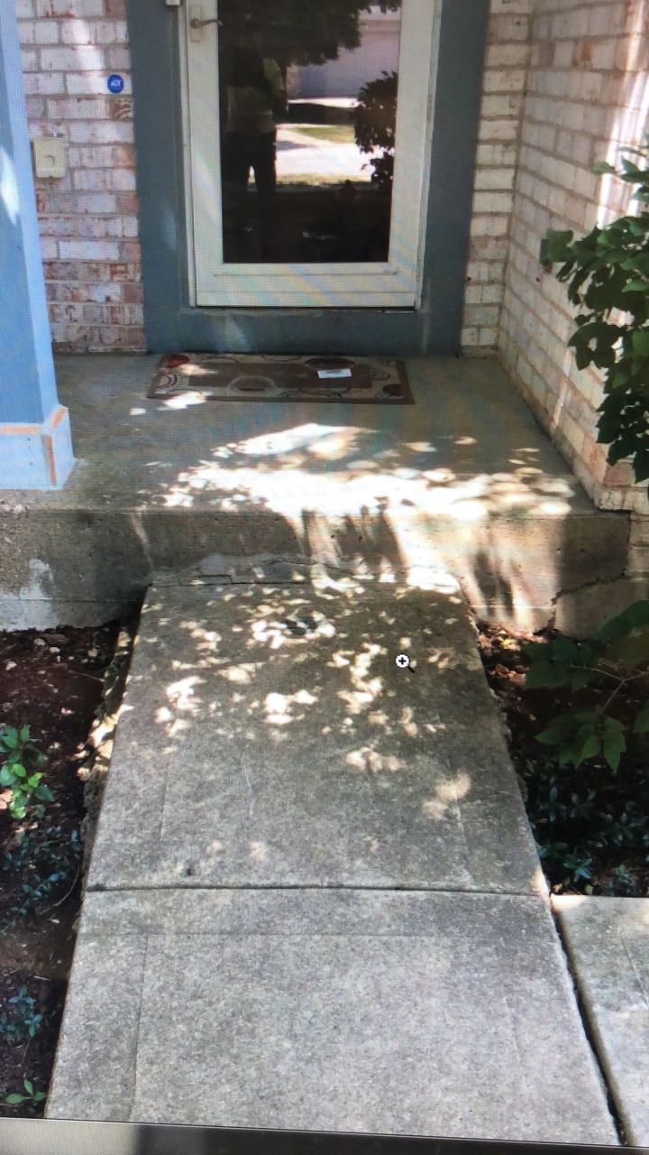 Concrete walkway leading to a front door with steps. Sunlight and shadows cover the path and door.